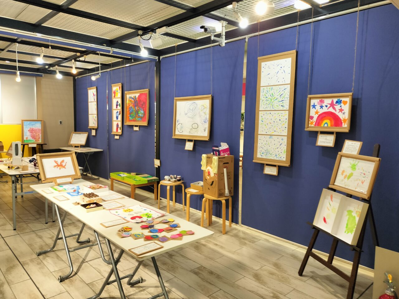青い壁面に飾られた子どもたちの絵画作品