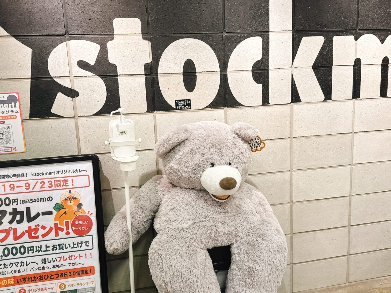 stockmartのロゴが壁に描かれた通路に置かれた大きなクマのぬいぐるみと告知看板