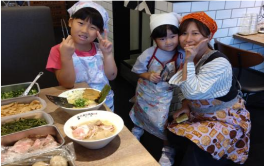 神奈川県・東京多摩エリアで展開する鶏とんこつ醤油ラーメン店「七志」では、毎月開催している体験型イベント「大人ラーメン教室」「親子ラーメン教室」が好評を博しています。運営する株式会社ナナシフードサービス（本社：横浜市青葉区）によると、累計受講者数は5,000人を突破し、昨年度比で150％の増加を記録したそうです。写真は親子で参加された方が完成したオリジナルラーメンを前に笑顔をみせている様子