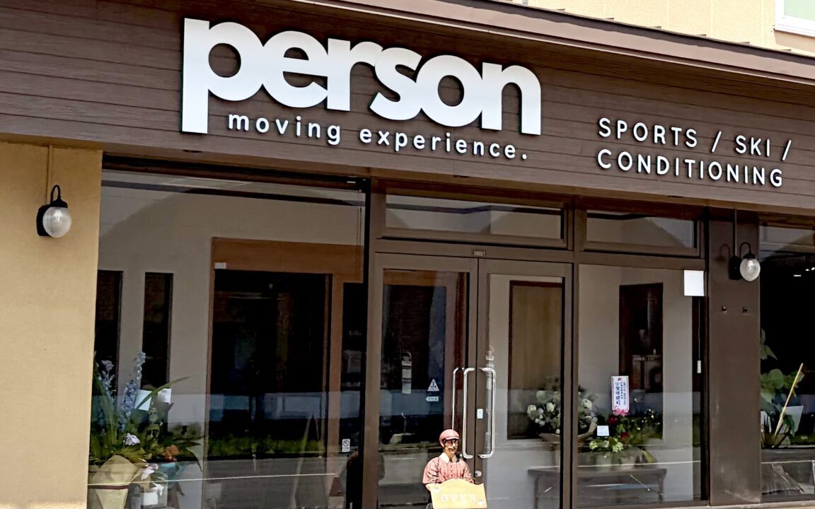 スポーツ専門店PERSON新店舗外観 北海道帯広市東4条南11丁目19番地3 郵便番号080-0804 2026年6月20日土曜日移転リニューアルオープン 元クックチャム帯広店跡地の建物 平屋建て 店舗入口の正面ガラス扉 自動ドア 青い看板 白い文字でPERSON スポーツショップ 十勝のスポーツパートナー ダイイチ東店のすぐ北側 道路沿いの店舗 営業中 駐車場あり NTTの大きな鉄塔から東へ進んだ場所 斉川漢方薬局の隣 帯広駅から車でアクセスしやすい立地 明るい昼間の写真 店舗正面の景色